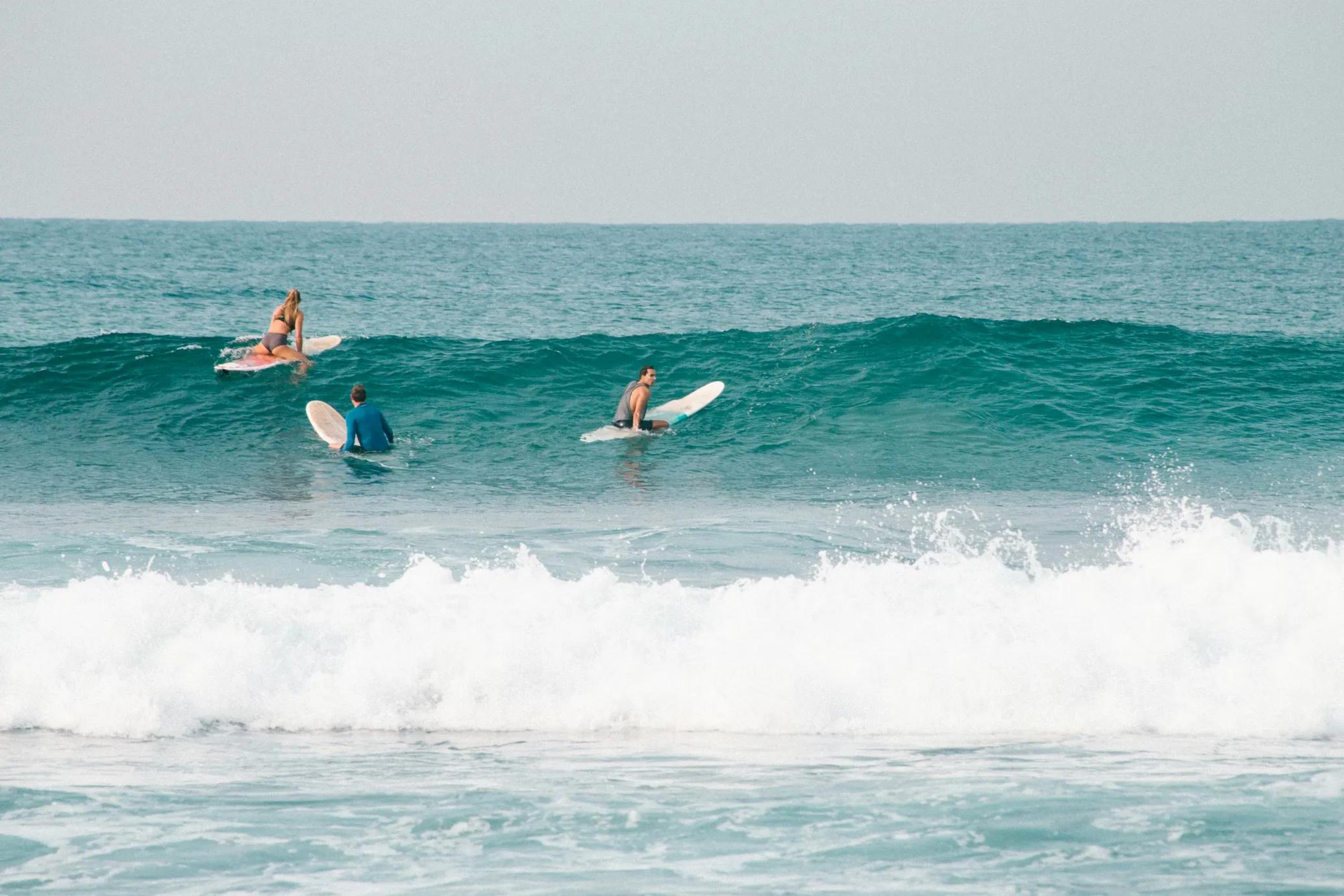 Group of 3 surfers, waiting to catch a wave in the ocean