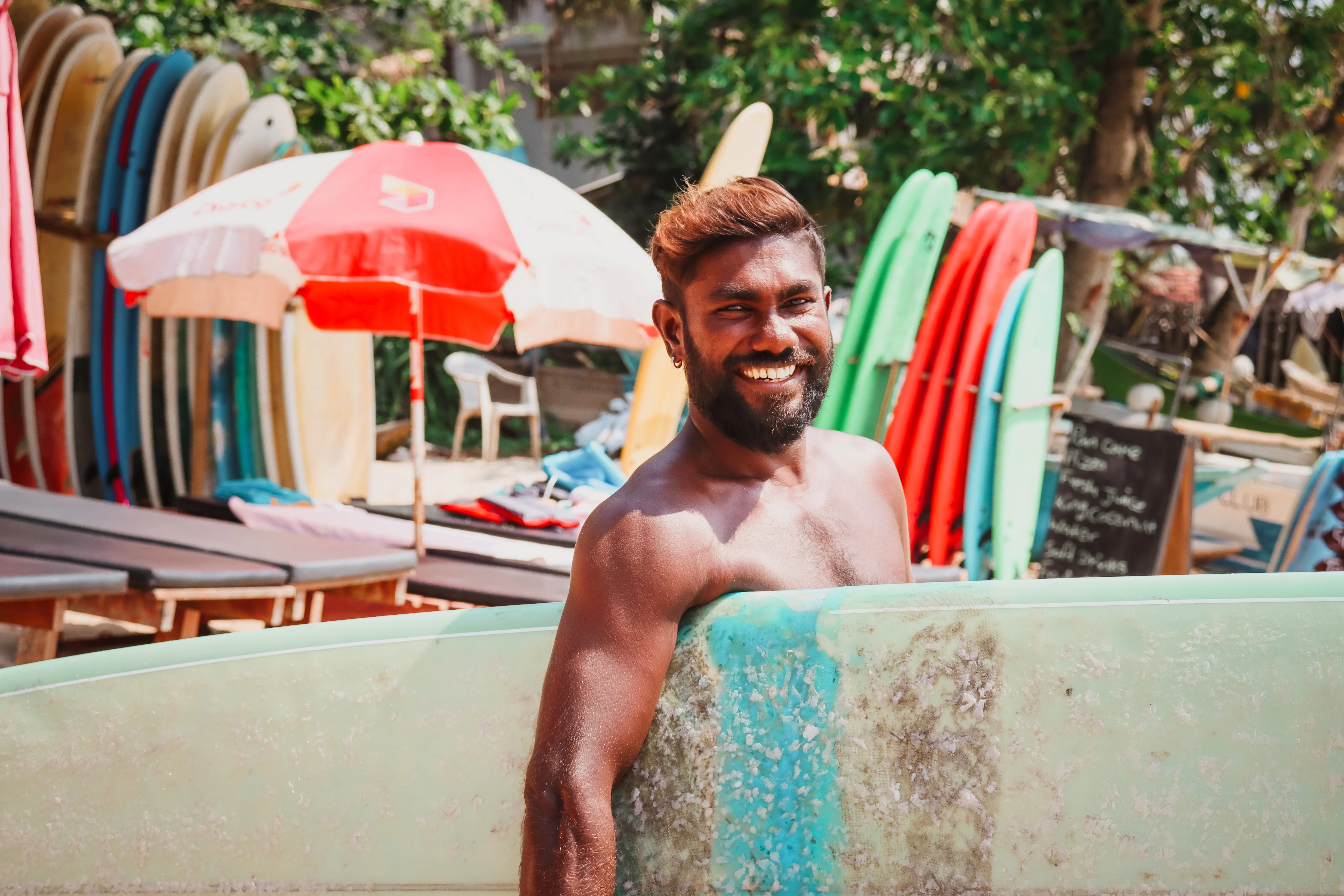 Lucky, certified surf instructor in Hiriketiya, holding a surfboard and smiling